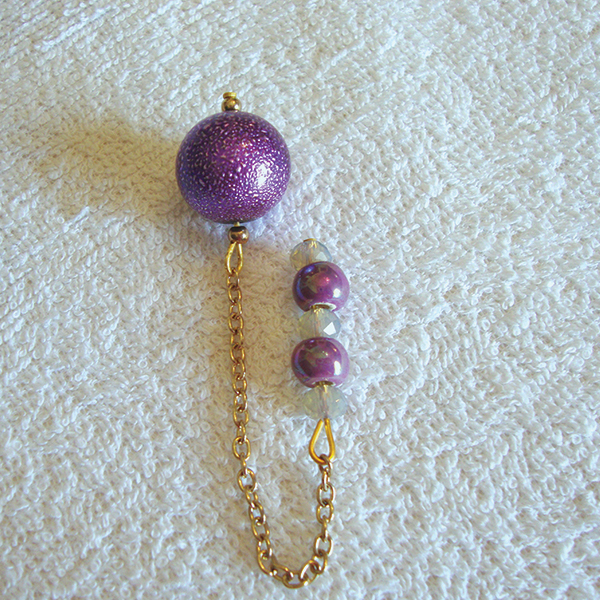 A purple foil round bead pendulum with a handle of 3 faceted milky crystals and 2 lilac ceramic beads