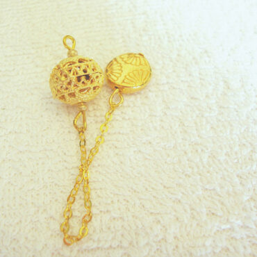 A Moroccan style gold plated dowsing pendulum with a hollow laced bead on a gold chain and a gold flower handle