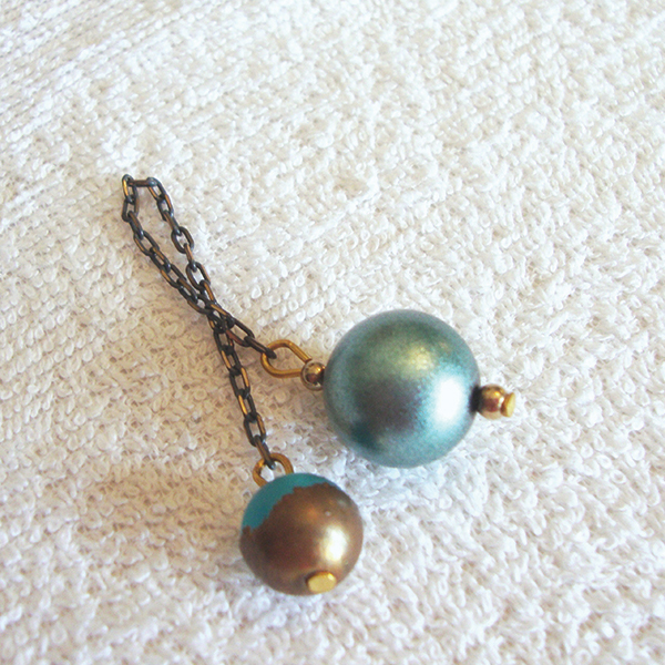 A metallic iridescent turquoise dowsing pendulum with a two-tone bead of turquoise-copper cap and an antique black-gold chain