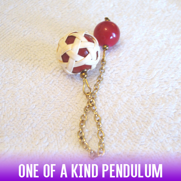 A red acrylic sphere dowsing pendulum in a white rattan knit style and a gold chain