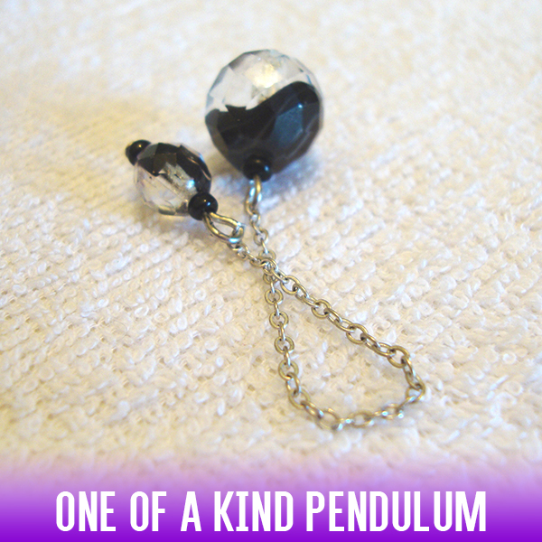 A dowsing pendulum of two-toned black & clear acrylic faceted sphere beads on a silver chain