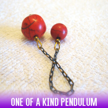 A dowsing pendulum made with natural red Howlite stone beads with dark veins and an antique dark black-gold chain.