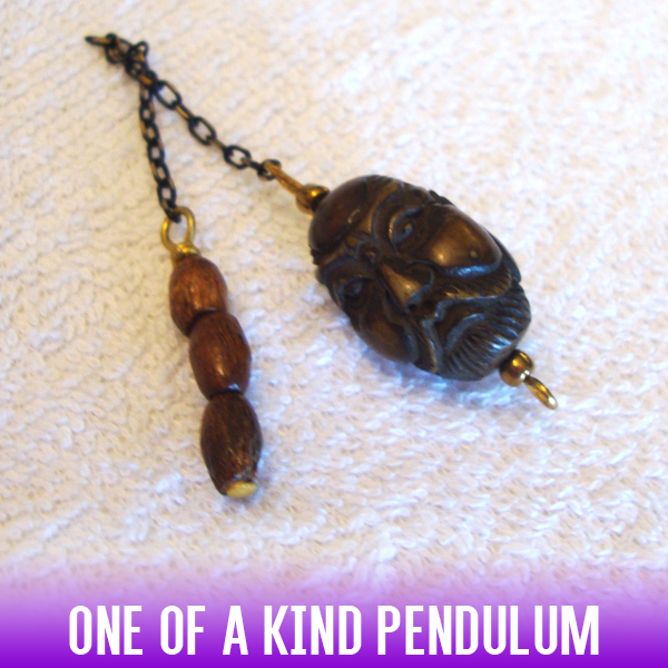An African-style oval dowsing pendulum made of hand-carved brown yak bone and a handle of three wooden beads. An antique black-gold chain completes the look