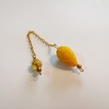 An small teardrop dowsing pendulum made of yellow hand-carved faux coral bead and a handle of a small clear colored bead with a hand-painted gold rose and a gold chain