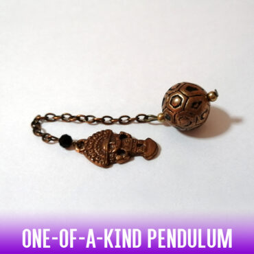 A dowsing pendulum made with a metallic antique style handmade carved copper round bead and a metallic copper vintage Aztec charm as a holder. A small black bead on the copper chain adds a spicy element.
